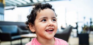 Cheerful young girl with curly hair smiling brightly in an indoor setting, exuding happiness.
