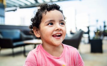 Cheerful young girl with curly hair smiling brightly in an indoor setting, exuding happiness.