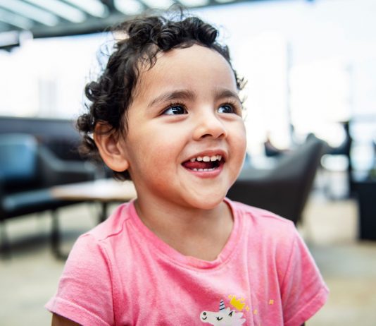 Cheerful young girl with curly hair smiling brightly in an indoor setting, exuding happiness.