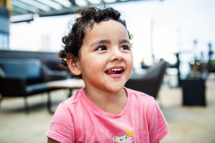 jersey-city-3-year-old-gabby-mateo-advances-in-tod Cheerful young girl with curly hair smiling brightly in an indoor setting, exuding happiness.
