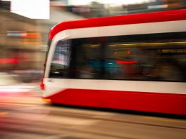 Blurred motion photo of a red tram speeding through city streets, capturing urban energy.