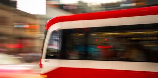 Blurred motion photo of a red tram speeding through city streets, capturing urban energy.
