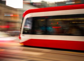Blurred motion photo of a red tram speeding through city streets, capturing urban energy.