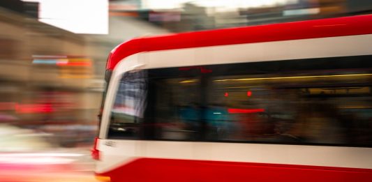 Blurred motion photo of a red tram speeding through city streets, capturing urban energy.