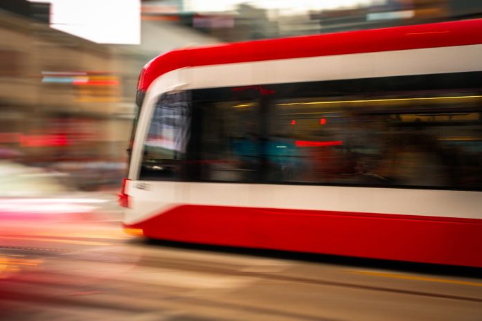 Blurred motion photo of a red tram speeding through city streets, capturing urban energy.