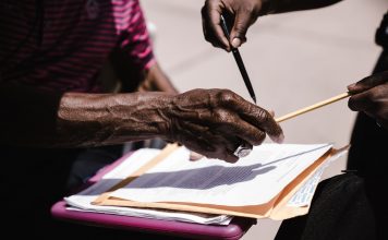 Close-up of hands exchanging documents with pens outdoors. Business agreement concept.
