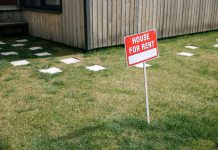 Jersey City Councilmen Move to Cap Rent Hikes in Tax-Abated Buildings A red 'House for Rent' sign stands on a grassy lawn beside a wooden house exterior.
