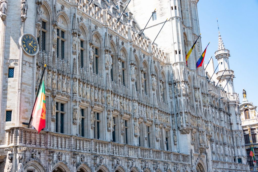A detailed view of the Gothic-style Town Hall in Brussels with flags and intricate stonework.