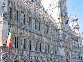 A detailed view of the Gothic-style Town Hall in Brussels with flags and intricate stonework.
