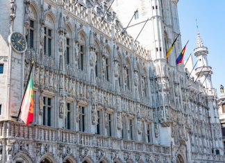 A detailed view of the Gothic-style Town Hall in Brussels with flags and intricate stonework.