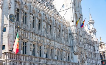 A detailed view of the Gothic-style Town Hall in Brussels with flags and intricate stonework.