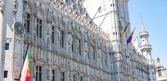 A detailed view of the Gothic-style Town Hall in Brussels with flags and intricate stonework.