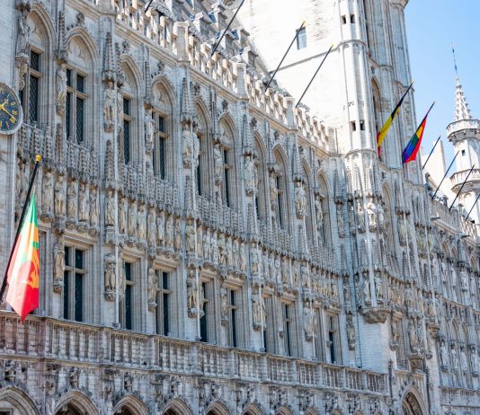 A detailed view of the Gothic-style Town Hall in Brussels with flags and intricate stonework.