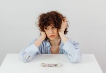 A woman in a blue blouse looks worried with a dollar bill on a table, symbolizing financial stress.