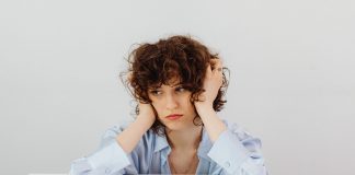 A woman in a blue blouse looks worried with a dollar bill on a table, symbolizing financial stress.