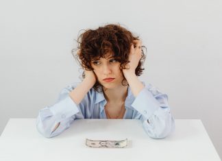 A woman in a blue blouse looks worried with a dollar bill on a table, symbolizing financial stress.