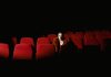 Jersey City’s Cultural Affairs Director Steps Down After 25 Years A woman sitting alone surrounded by empty red theater seats in a dark auditorium.