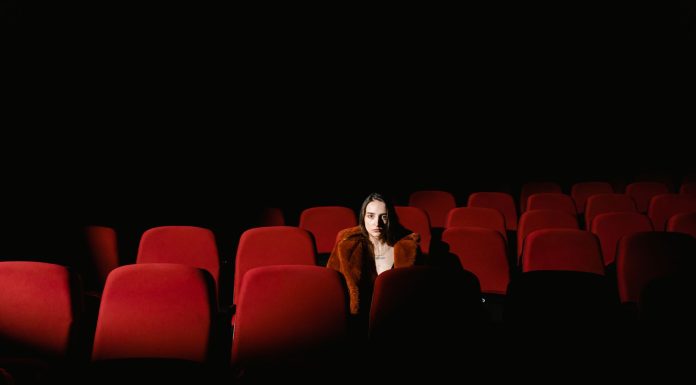 Jersey City’s Cultural Affairs Director Steps Down After 25 Years A woman sitting alone surrounded by empty red theater seats in a dark auditorium.
