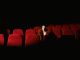 Jersey City’s Cultural Affairs Director Steps Down After 25 Years A woman sitting alone surrounded by empty red theater seats in a dark auditorium.