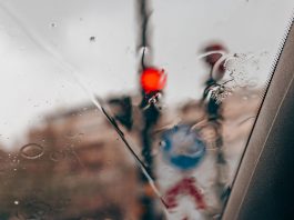 Jersey City’s Parking Nightmares Hit the Edinburgh Fringe Stage Blurred red traffic light seen through raindrops on a car windshield in a city setting.