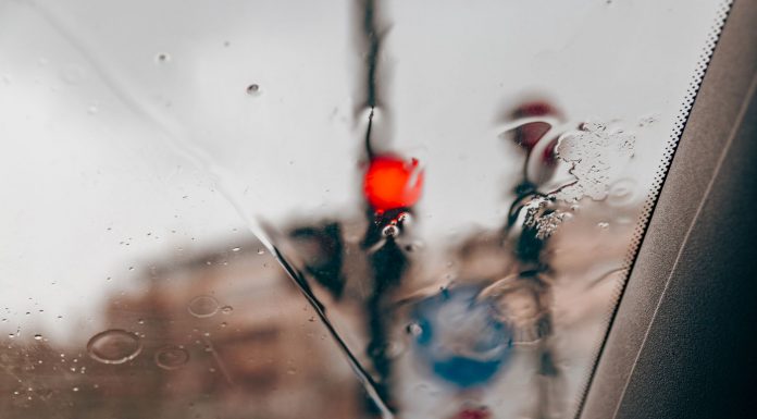 Blurred red traffic light seen through raindrops on a car windshield in a city setting.