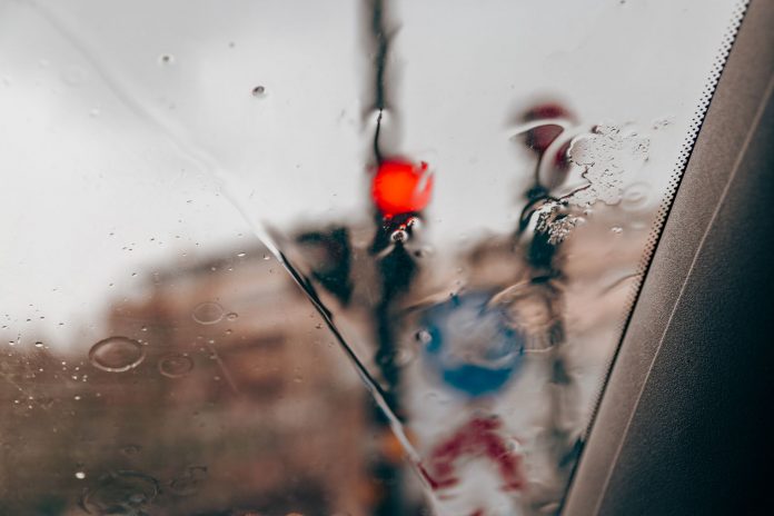 jersey-city-s-parking-nightmares-hit-the-edinburgh Blurred red traffic light seen through raindrops on a car windshield in a city setting.