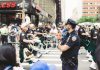 A police officer oversees a marching band parade in a busy urban street setting.