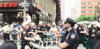 A police officer oversees a marching band parade in a busy urban street setting.