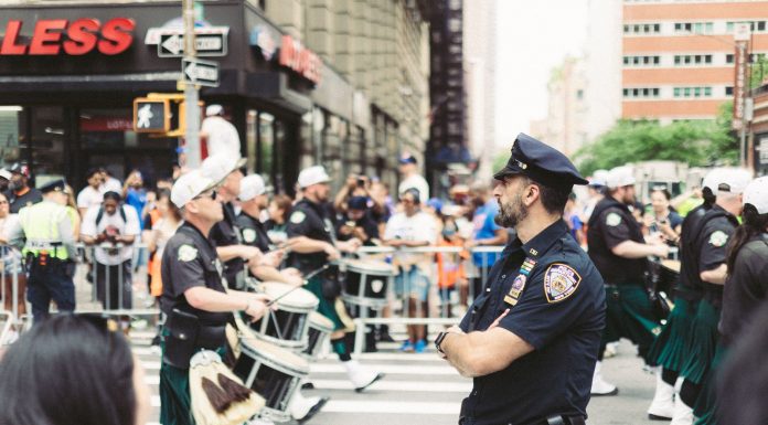A police officer oversees a marching band parade in a busy urban street setting.
