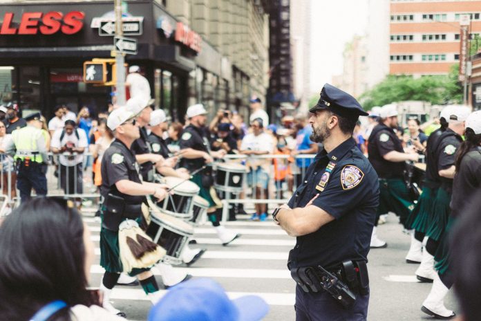 A police officer oversees a marching band parade in a busy urban street setting.