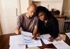 A couple sitting at a table reviewing financial documents, highlighting domestic budgeting.
