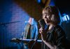Smiling caucasian woman singing with vintage microphone during live music performance.