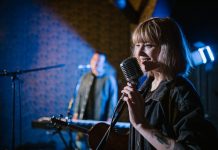 Smiling caucasian woman singing with vintage microphone during live music performance.