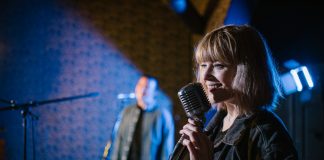 Smiling caucasian woman singing with vintage microphone during live music performance.
