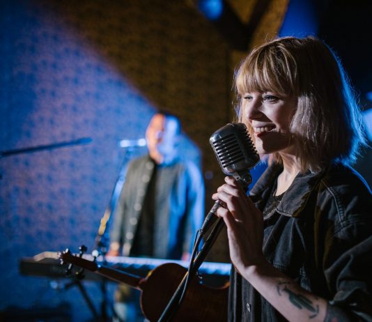 Smiling caucasian woman singing with vintage microphone during live music performance.