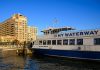 NY Waterway ferry docking at Hoboken, NJ against a clear blue sky, showcasing urban architecture.