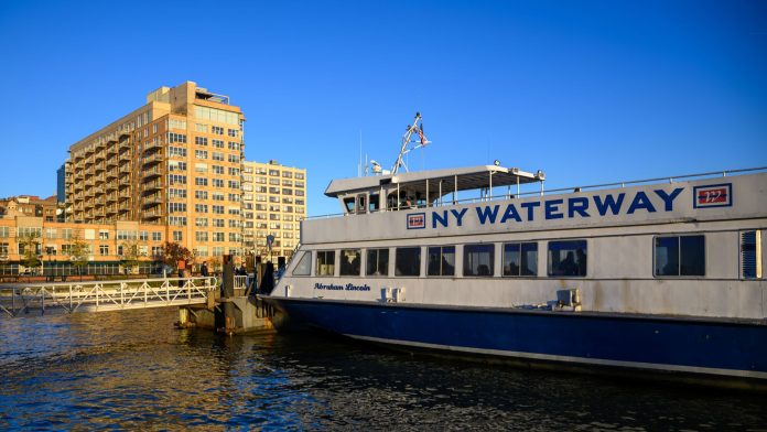 NY Waterway ferry docking at Hoboken, NJ against a clear blue sky, showcasing urban architecture.