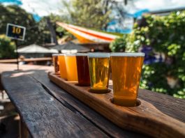 ÚLTIMA HORA: 7 Lugares para Probar Flights en Hoboken y Jersey City A vibrant beer flight displayed on a rustic wood table outdoors during a sunny day.