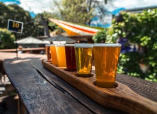 A vibrant beer flight displayed on a rustic wood table outdoors during a sunny day.
