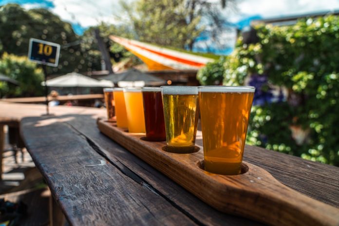 A vibrant beer flight displayed on a rustic wood table outdoors during a sunny day.