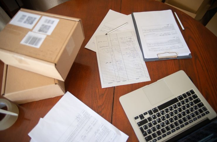 Flat lay of a workspace with laptop, documents, and cardboard boxes for e-commerce operations.