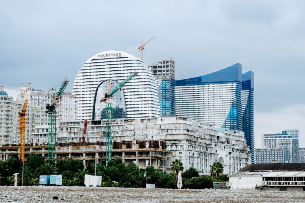 A modern waterfront cityscape showcasing construction cranes and urban skyline under a cloudy sky.