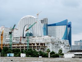 A modern waterfront cityscape showcasing construction cranes and urban skyline under a cloudy sky.