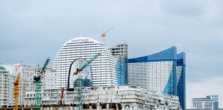 A modern waterfront cityscape showcasing construction cranes and urban skyline under a cloudy sky.