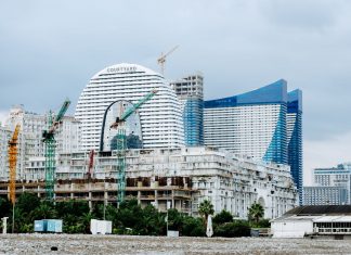 ÚLTIMA HORA: Aprueban complejo de 17 pisos con hotel en Marin Boulevard A modern waterfront cityscape showcasing construction cranes and urban skyline under a cloudy sky.