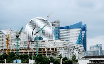 A modern waterfront cityscape showcasing construction cranes and urban skyline under a cloudy sky.