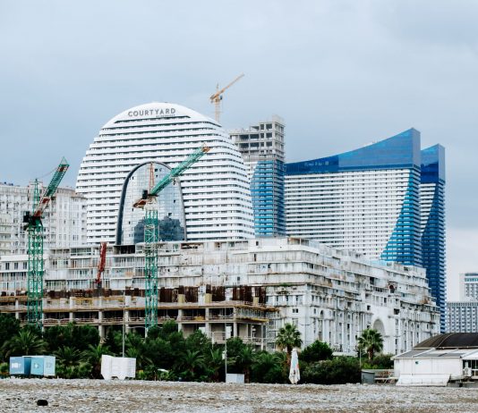 A modern waterfront cityscape showcasing construction cranes and urban skyline under a cloudy sky.