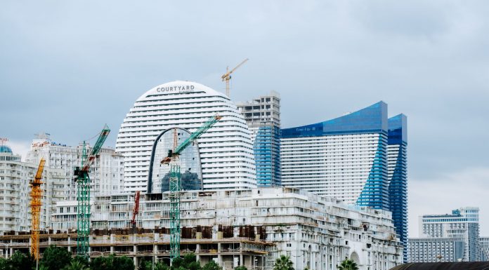 A modern waterfront cityscape showcasing construction cranes and urban skyline under a cloudy sky.