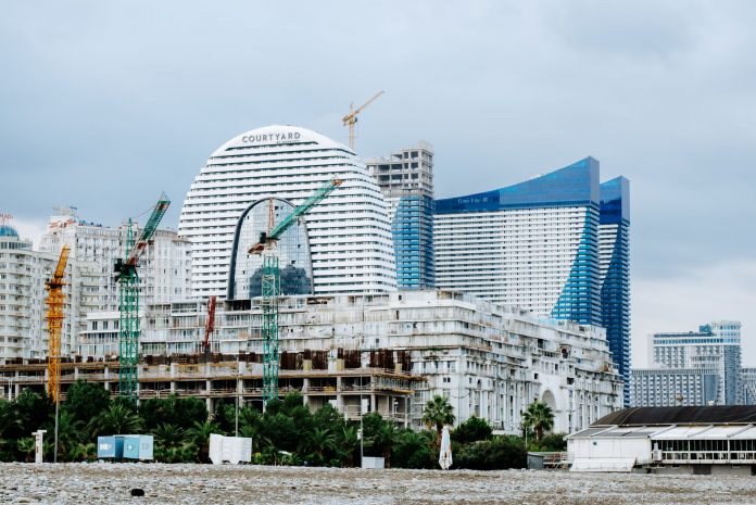ltima-hora-aprueban-complejo-de-17-pisos-con-hote A modern waterfront cityscape showcasing construction cranes and urban skyline under a cloudy sky.