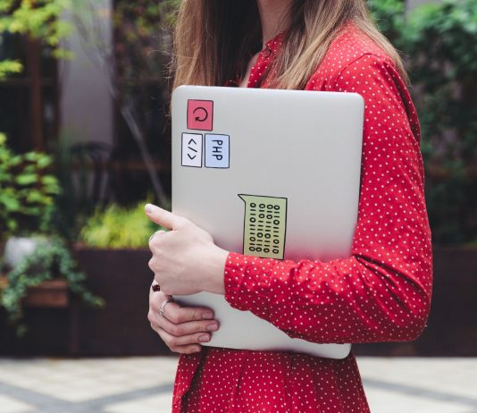 ÚLTIMA HORA: Hopeworks abre centro de desarrollo laboral en Newark A young woman in a red polka dot shirt holds a laptop with stickers outdoors.